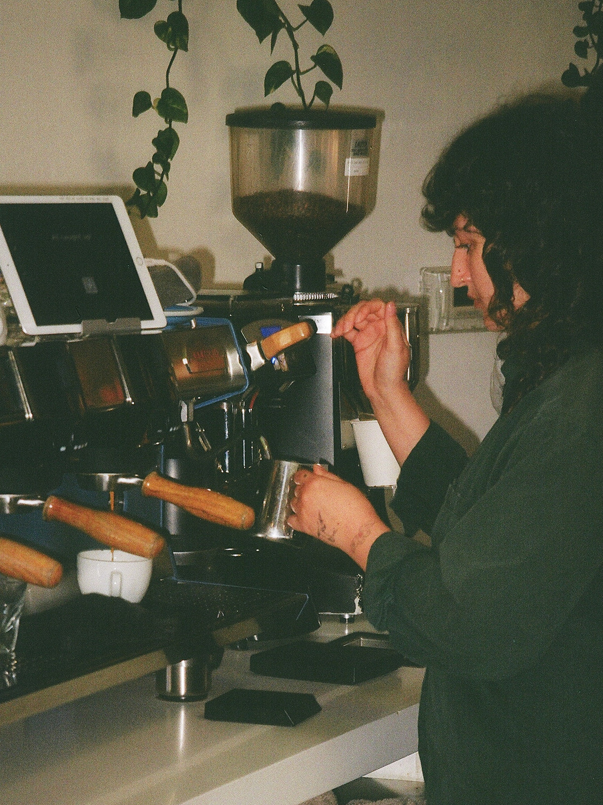 A close-up shot of a female barista steaming a silver pitcher of milk while a shot of espresso drips into a white porcelain cup